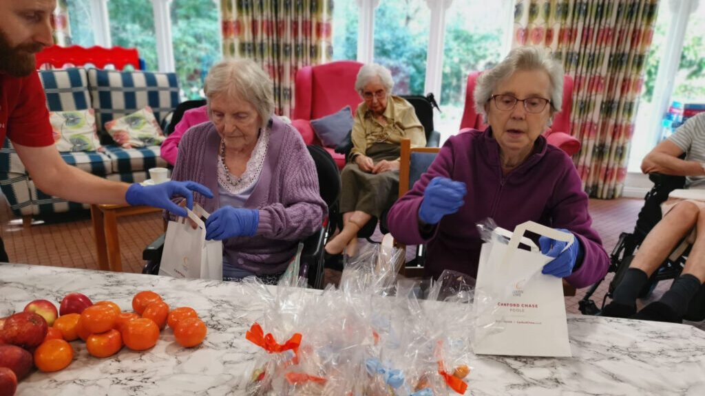 Seated left and right at the table respectively, Canford Chase residents Barbara Rivett and Marjory Jewkes help prepare the packed lunches for Poole food bank
